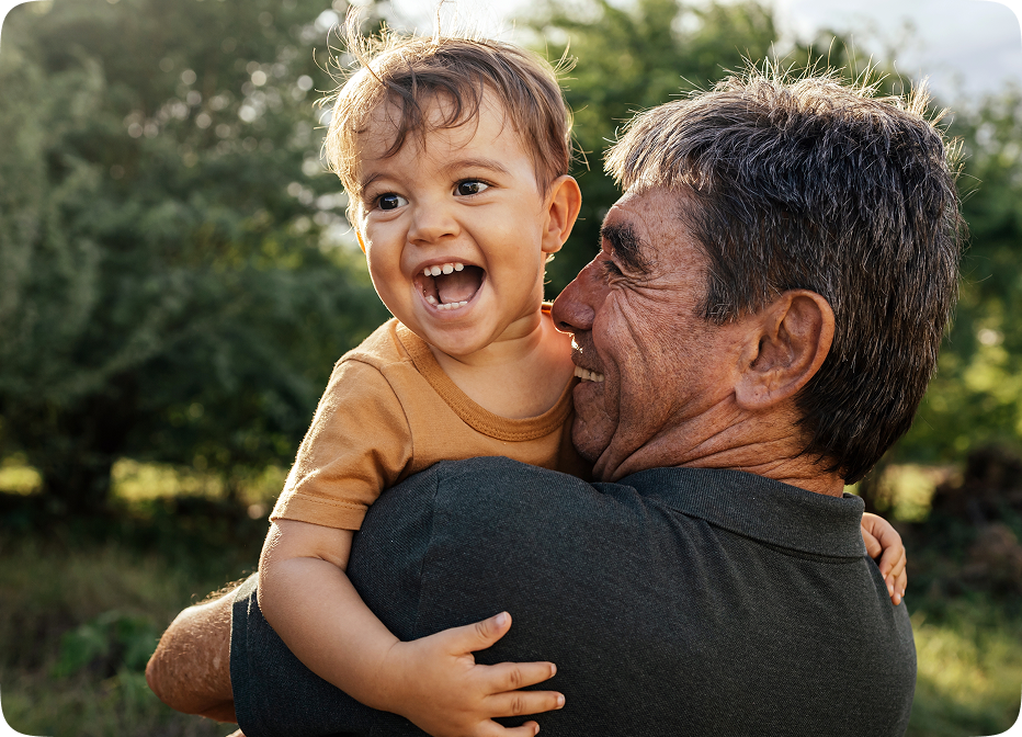 Happy grandfather holding laughing grandchild outdoors, symbolizing joyful moments supported by Audien hearing aids